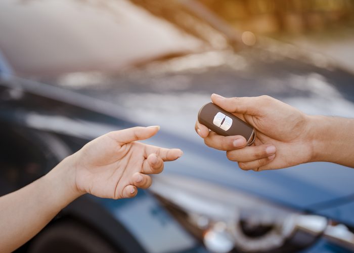Close up woman holding new car systems key of blue hatchback car after buying from dealer at outdoor.